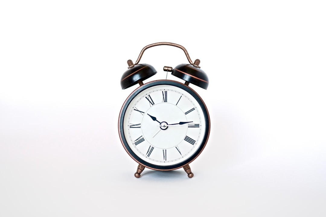 An alarm clock on a bedside table in soft morning light, showing the gap between weekday wake times and weekend sleep schedules